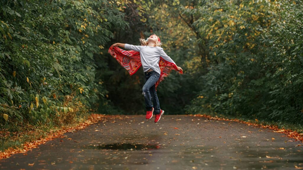 Little girl jumping with a red scarf as a cape